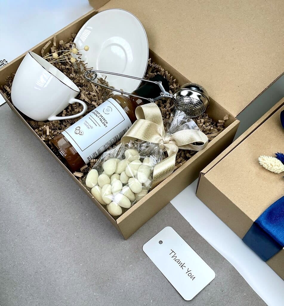 gotowy do wręczenia prezent zestaw box prezentowy a w środku filiżanka, stylowy zaparzacz do herbaty naturalny przepyszny syrop z orzechów laskowych migdały w białej czekoladzie z kokosem