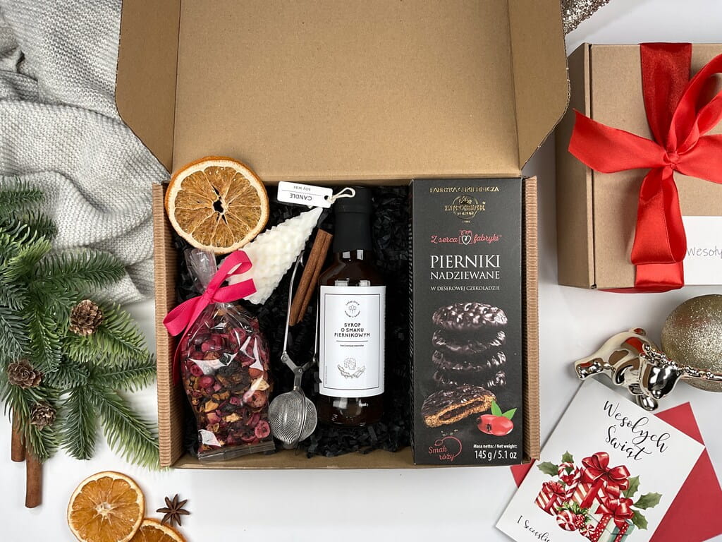Świąteczny box prezentowy z herbatą żurawinową, zaparzaczem, świecą sojową w kształcie choinki, syropem piernikowym, pierniczkami nadziewanymi różą w ciemnej czekoladzie i ozdobami świątecznymi. Idealny pod choinkę i na Mikołajki.