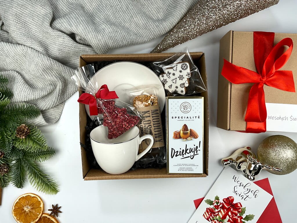 Elegancki prezent na Mikołaja i święta: filiżanka porcelanowa, gorzka czekolada choinka z malinami, migdały w złotej czekoladzie, baton miodowy i pierniczek. Świąteczny box premium.