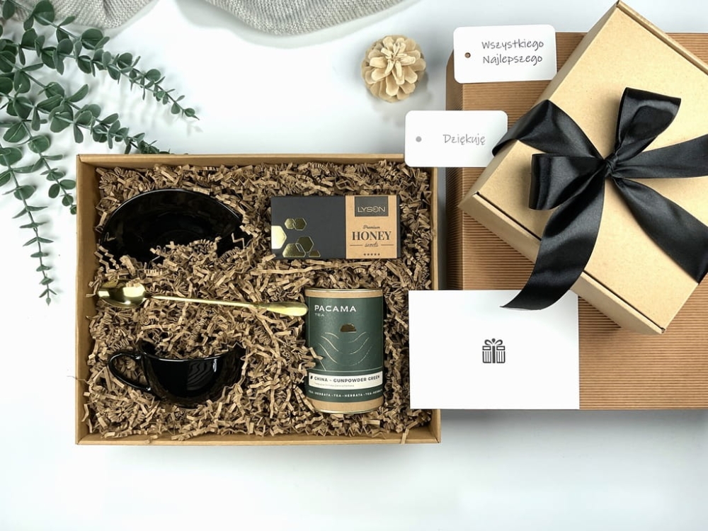 Box prezentowy z czarną filiżanką, złotą łyżeczką, zieloną herbatą i krówkami miodowymi. Elegancki zestaw świąteczny, idealny dla bliskich, pracowników i nauczycieli.