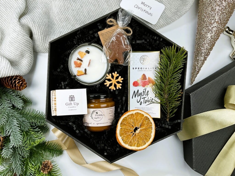 Świąteczny zestaw z aromatyczną świecą sojową, słodkim czekoladowym ludkiem, migdałami w różowej czekoladzie, miodem cynamonowym i dekoracyjnymi zapałkami.