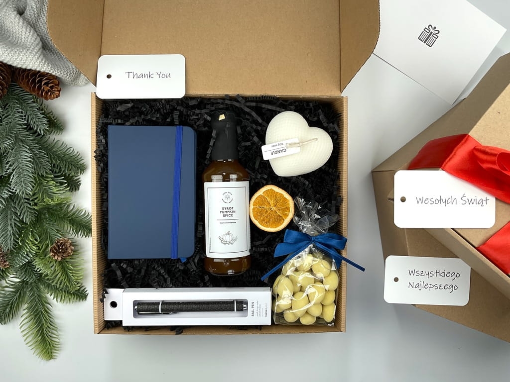 prezent box upominek który zwiera: niebieski skórzany notatnik, czarny elegancki długopis, przepyszny naturalny syrop do kawy o smaku dyniowym, migdały w mlecznej czekoladzie i naturalna świeca sojowa