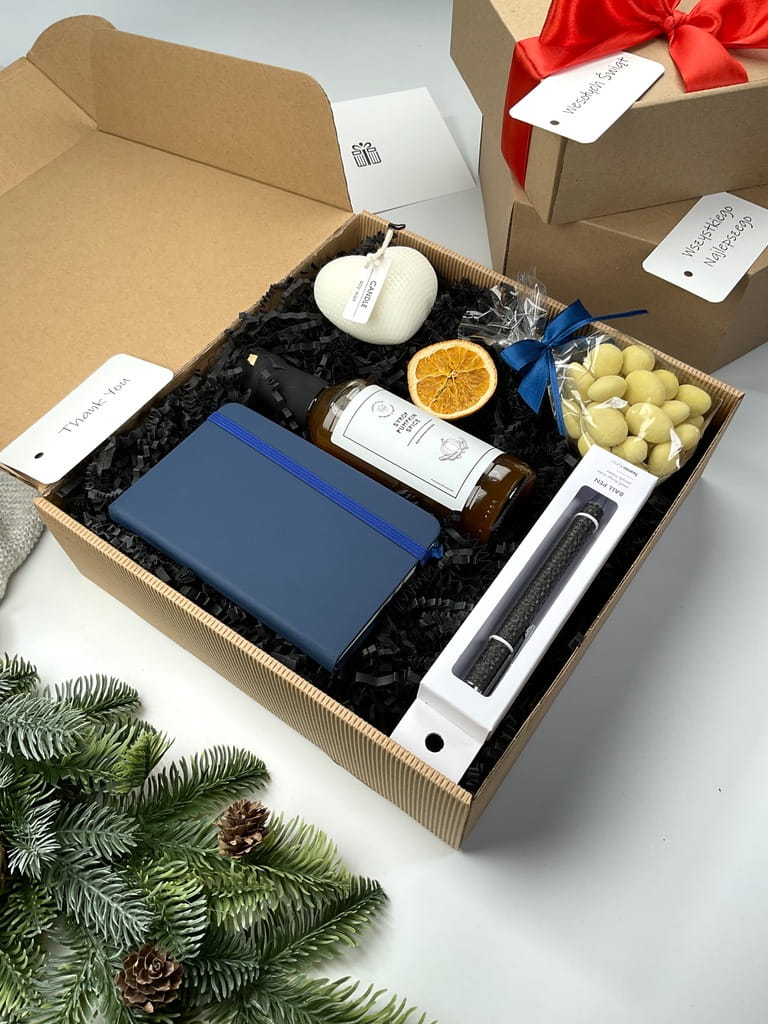 prezent box upominek który zwiera: niebieski skórzany notatnik, czarny elegancki długopis, przepyszny naturalny syrop do kawy o smaku dyniowym, migdały w mlecznej czekoladzie i naturalna świeca sojowa