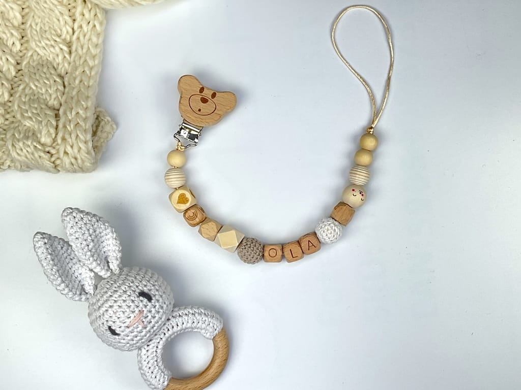 Ręcznie robiona zawieszka do smoczka z imieniem z naturalnego drewna bukowego i świerkowego. Personalizowana, ekologiczna zawieszka z drewnianych koralików, bawełnianej nitki i mocnego sznurka. Idealna na prezent dla dziecka.