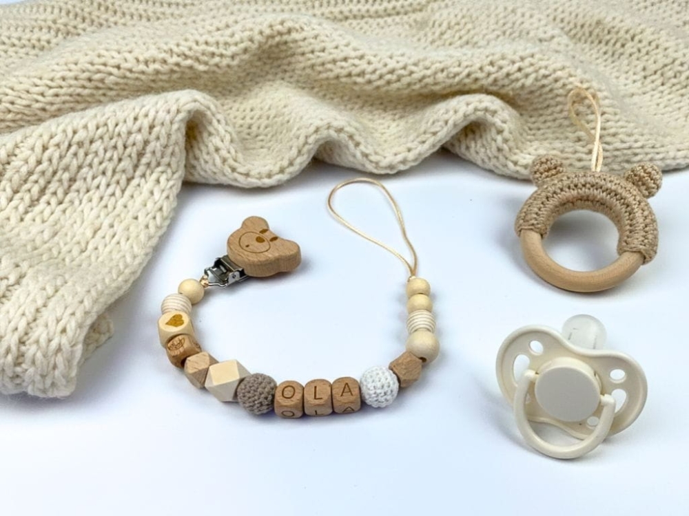 Ręcznie robiona zawieszka do smoczka z imieniem z naturalnego drewna bukowego i świerkowego. Personalizowana, ekologiczna zawieszka z drewnianych koralików, bawełnianej nitki i mocnego sznurka. Idealna na prezent dla dziecka.
