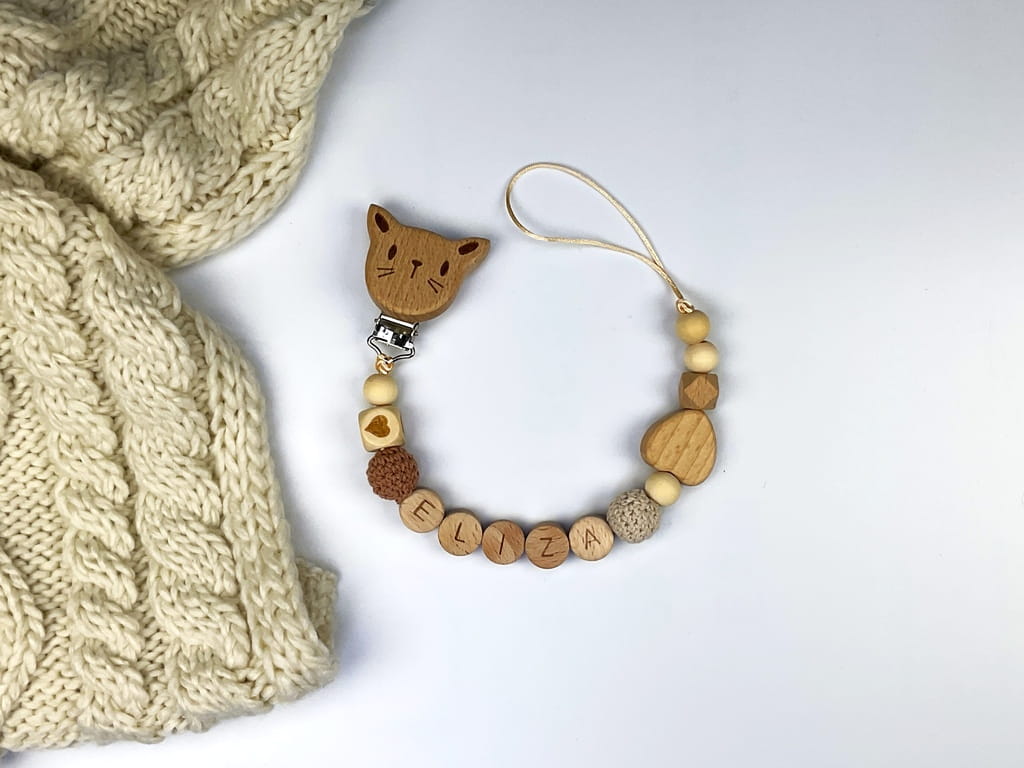 Ręcznie robiona zawieszka do smoczka z imieniem z naturalnego drewna bukowego i świerkowego. Personalizowana, ekologiczna zawieszka z drewnianych koralików, bawełnianej nitki i mocnego sznurka. Idealna na prezent dla dziecka.