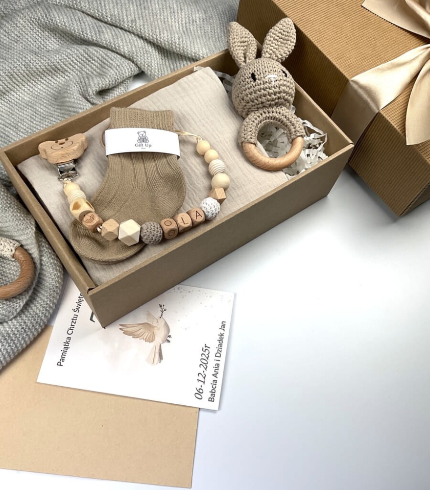 Zestaw prezentowy na chrzest dla chłopca: muślinowa pieluszka, ręcznie robiona grzechotka, zawieszka na smoczek, drewniana zawieszka z imieniem, skarpetki i personalizowana kartka.