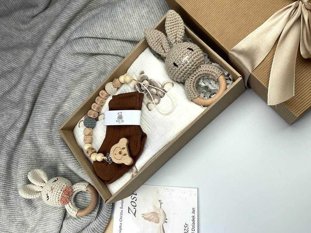 Zestaw prezentowy na chrzest dla chłopca: muślinowa pieluszka, ręcznie robiona grzechotka, zawieszka na smoczek, drewniana zawieszka z imieniem, skarpetki i personalizowana kartka.