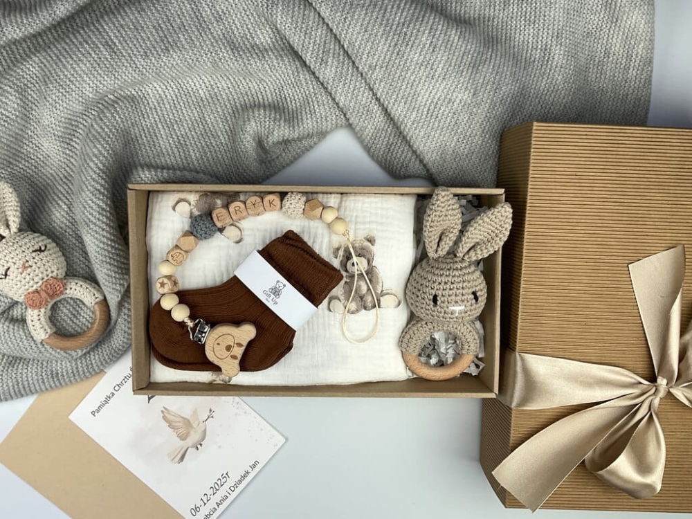 Zestaw prezentowy na chrzest dla chłopca: muślinowa pieluszka, ręcznie robiona grzechotka, zawieszka na smoczek, drewniana zawieszka z imieniem, skarpetki i personalizowana kartka.