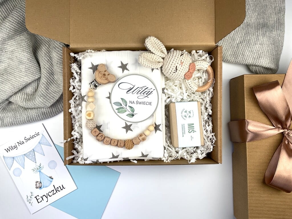 Zestaw prezentowy na chrzest dla chłopca: muślinowa pieluszka, ręcznie robiona grzechotka, zawieszka na smoczek, drewniana zawieszka z imieniem, skarpetki i personalizowana kartka.