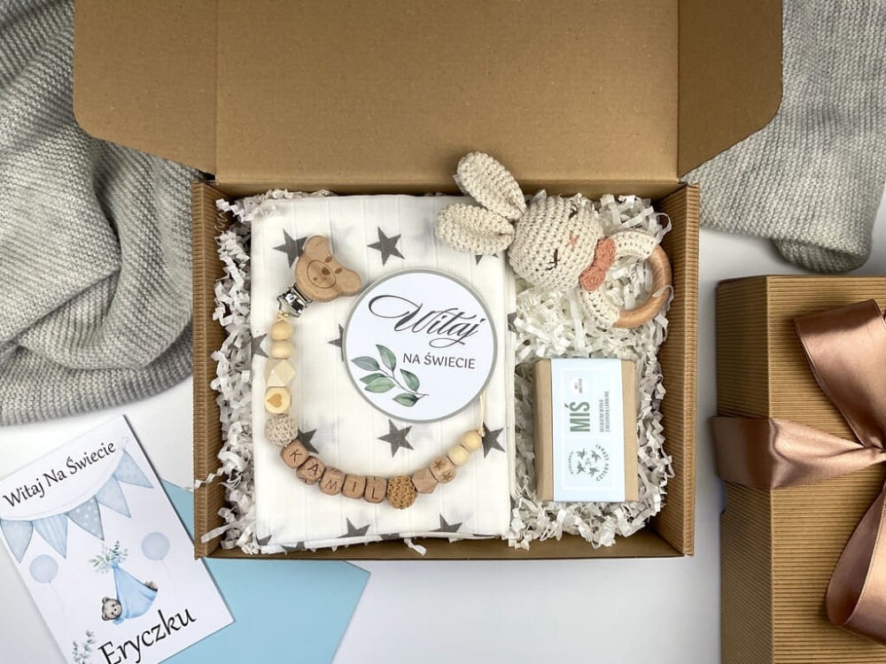 Zestaw prezentowy na chrzest dla chłopca: muślinowa pieluszka, ręcznie robiona grzechotka, zawieszka na smoczek, drewniana zawieszka z imieniem, skarpetki i personalizowana kartka.