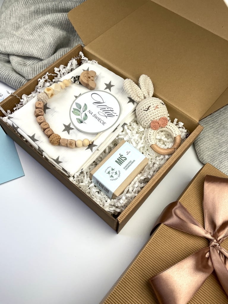 Zestaw prezentowy na chrzest dla chłopca: muślinowa pieluszka, ręcznie robiona grzechotka, zawieszka na smoczek, drewniana zawieszka z imieniem, skarpetki i personalizowana kartka.
