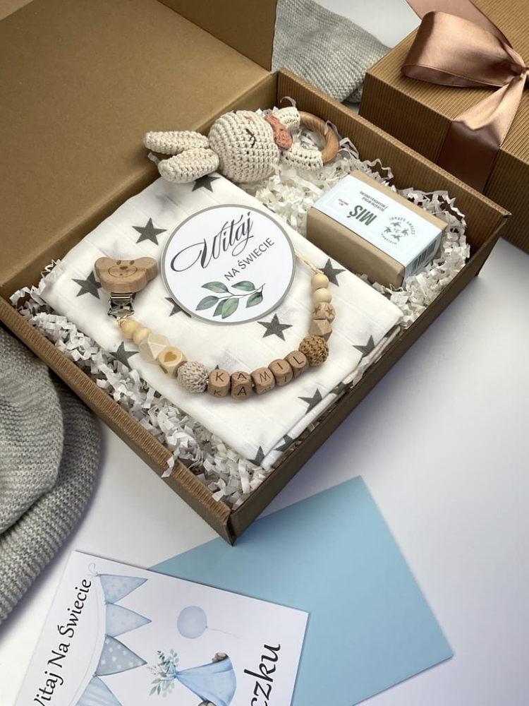 Zestaw prezentowy na chrzest dla chłopca: muślinowa pieluszka, ręcznie robiona grzechotka, zawieszka na smoczek, drewniana zawieszka z imieniem, skarpetki i personalizowana kartka.