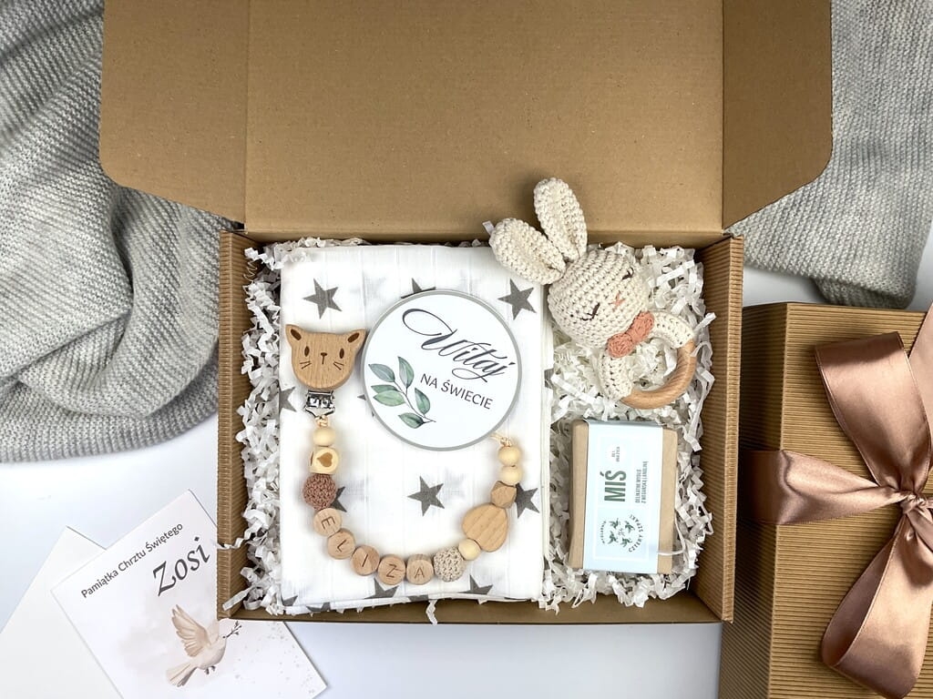 Zestaw prezentowy na chrzest dla chłopca: muślinowa pieluszka, ręcznie robiona grzechotka, zawieszka na smoczek, drewniana zawieszka z imieniem, skarpetki i personalizowana kartka.