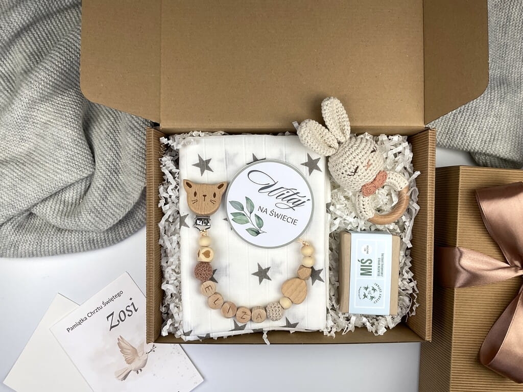Zestaw prezentowy na chrzest dla chłopca: muślinowa pieluszka, ręcznie robiona grzechotka, zawieszka na smoczek, drewniana zawieszka z imieniem, skarpetki i personalizowana kartka.