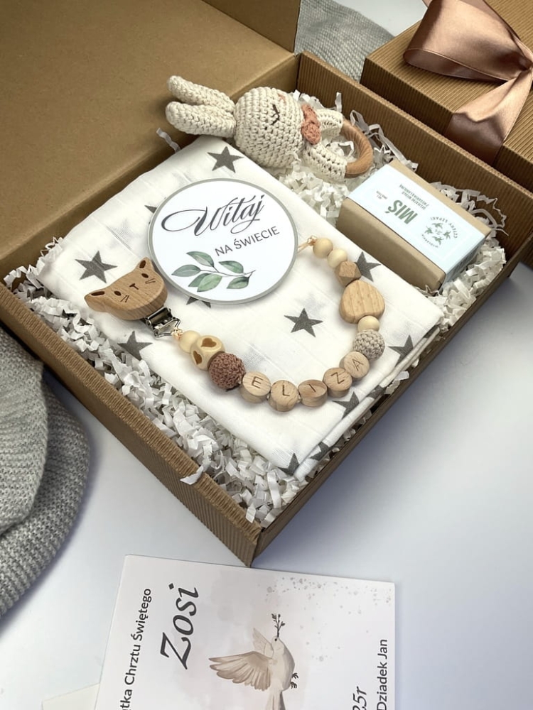 Zestaw prezentowy na chrzest dla chłopca: muślinowa pieluszka, ręcznie robiona grzechotka, zawieszka na smoczek, drewniana zawieszka z imieniem, skarpetki i personalizowana kartka.