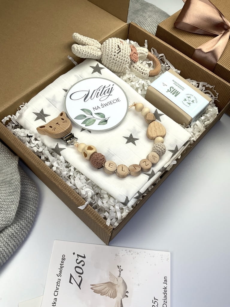 Zestaw prezentowy na chrzest dla chłopca: muślinowa pieluszka, ręcznie robiona grzechotka, zawieszka na smoczek, drewniana zawieszka z imieniem, skarpetki i personalizowana kartka.