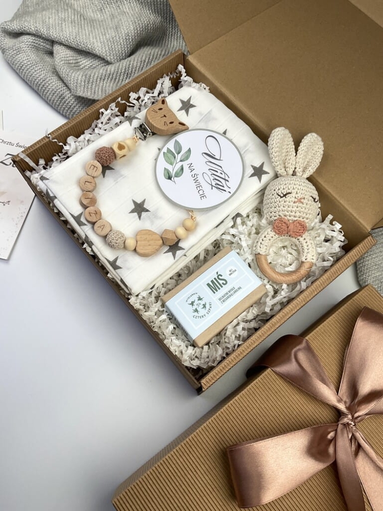 Zestaw prezentowy na chrzest dla chłopca: muślinowa pieluszka, ręcznie robiona grzechotka, zawieszka na smoczek, drewniana zawieszka z imieniem, skarpetki i personalizowana kartka.