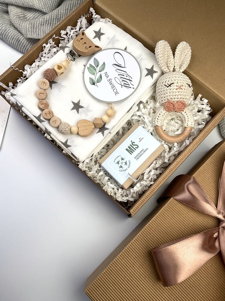 Zestaw prezentowy na chrzest dla chłopca: muślinowa pieluszka, ręcznie robiona grzechotka, zawieszka na smoczek, drewniana zawieszka z imieniem, skarpetki i personalizowana kartka.