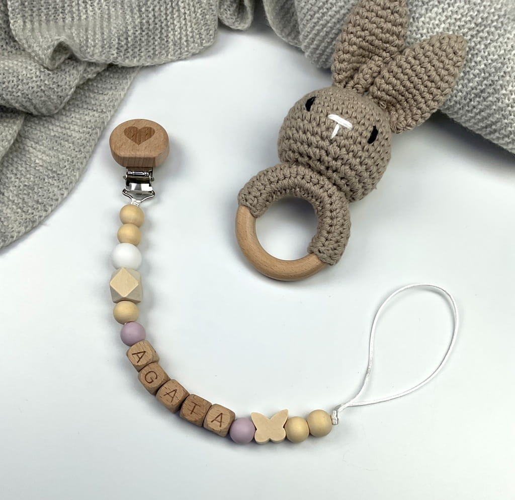 Ręcznie robiona zawieszka do smoczka z drewnianych koralików. Personalizowana imieniem dziecka, bezpieczna i stylowa. Idealny dodatek dla niemowląt i wyjątkowy pomysł na prezent.