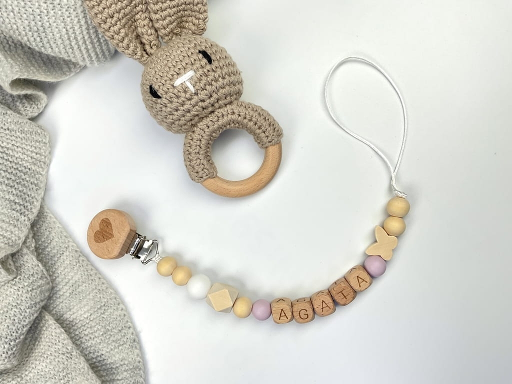 Ręcznie robiona zawieszka do smoczka z drewnianych koralików. Personalizowana imieniem dziecka, bezpieczna i stylowa. Idealny dodatek dla niemowląt i wyjątkowy pomysł na prezent.