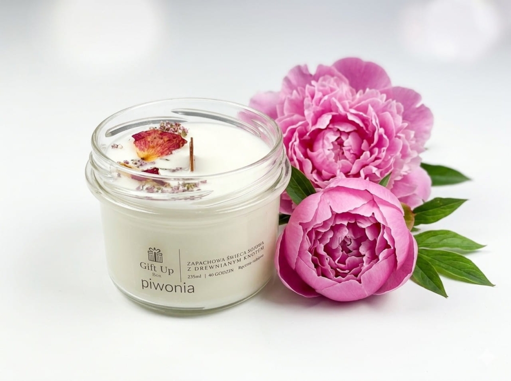 Ręcznie robiona świeca zapachowa o aromacie piwonii obok wanny i ręczników. Domowe SPA z naturalną świecą sojową. Kwiatowy zapach do kąpieli, który odpręża i wprowadza romantyczny nastrój w łazience.