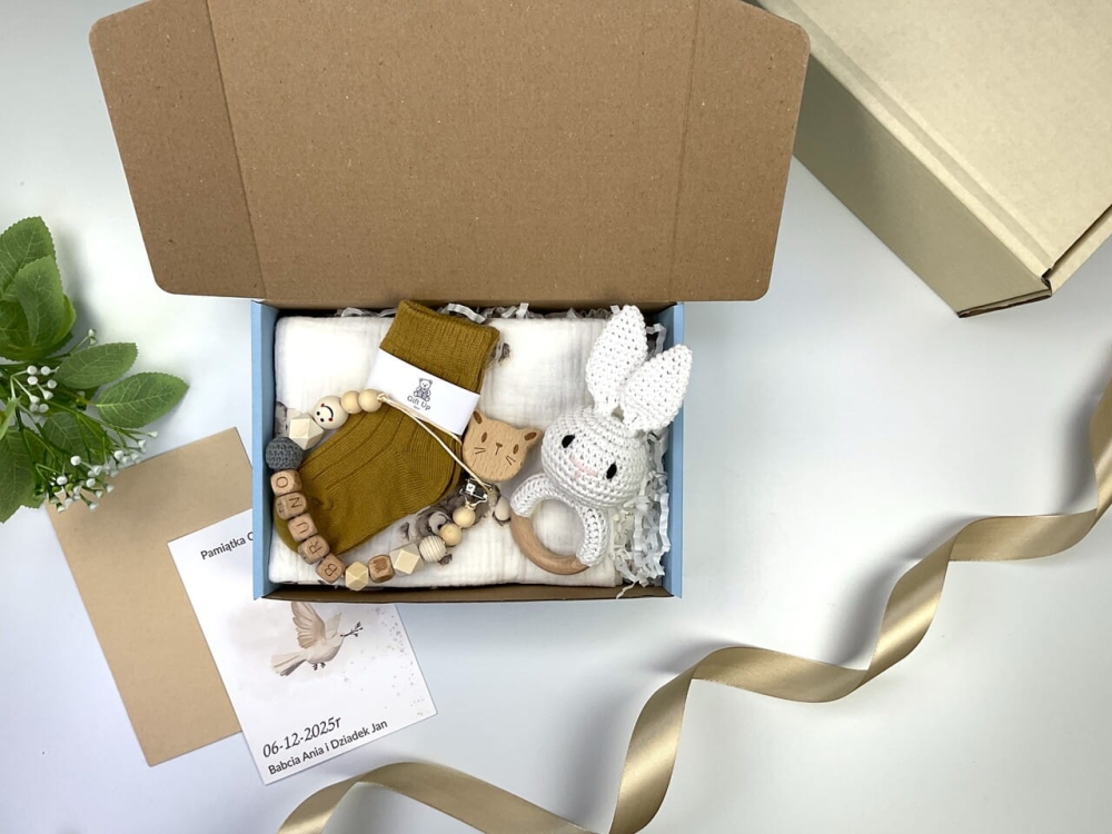 Zestaw prezentowy na chrzest dla chłopca: muślinowa pieluszka, ręcznie robiona grzechotka, zawieszka na smoczek, drewniana zawieszka z imieniem, skarpetki i personalizowana kartka.