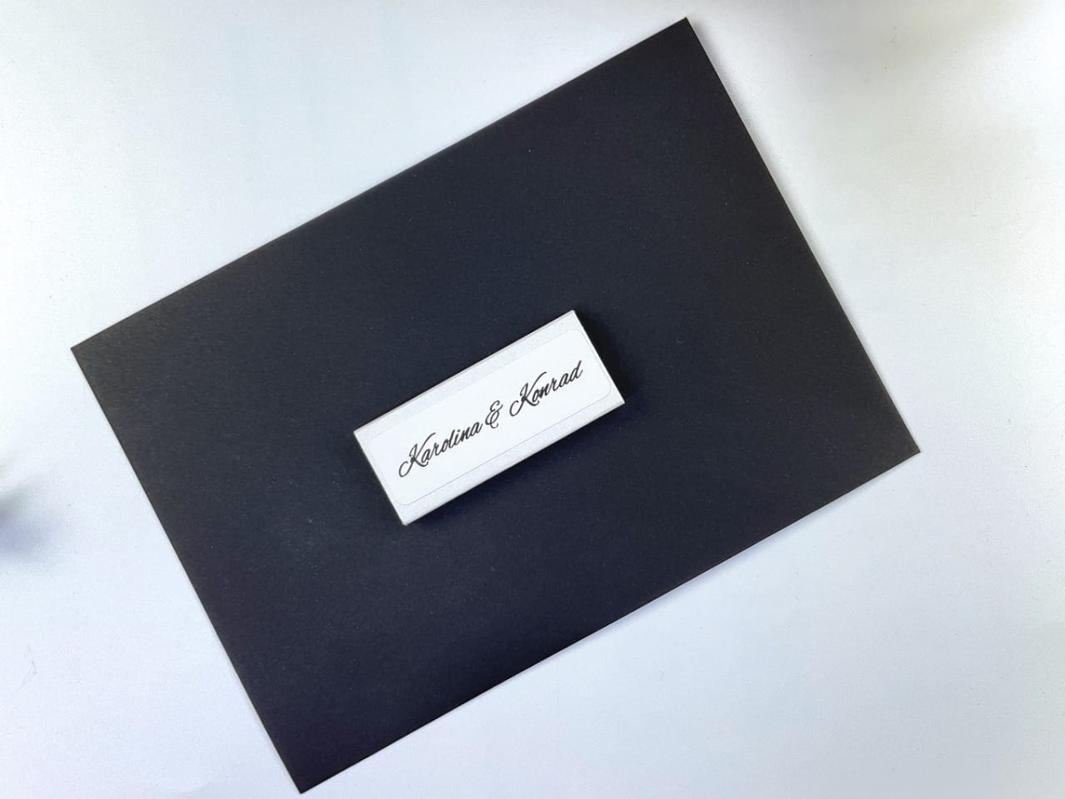 Otwarte białe pudełko zapałek o wymiarach 56x24x8 mm z widocznymi zapałkami o długości 47 mm. Spersonalizowany gadżet z nadrukiem na czarnym tle.